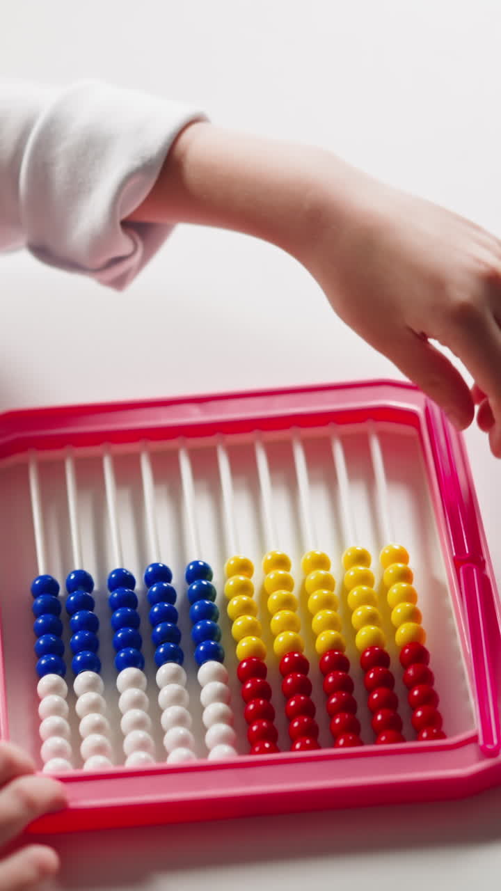 Smart little girl student pours plastic beads and puts stick to abacus frame at home mental arithmetic lesson upper closeup slow motion