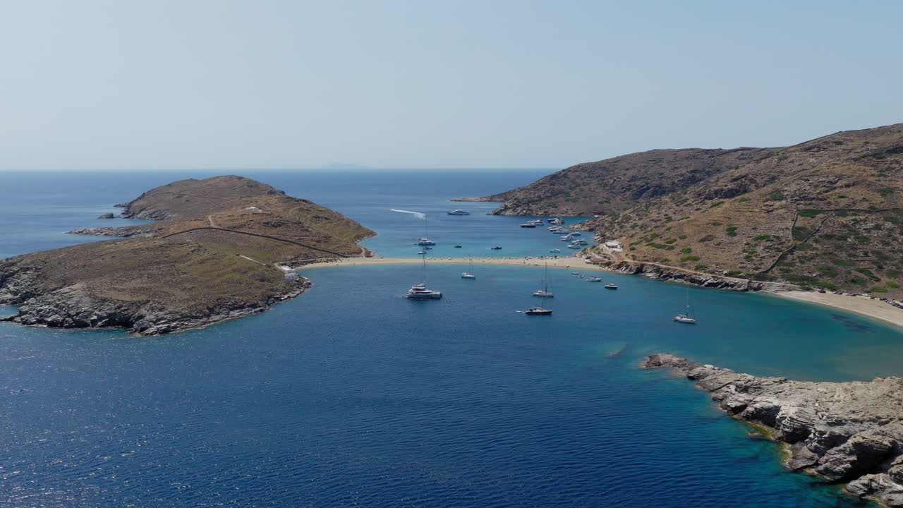 Slow panning drone shot of yachts and sailboats moored around the iconic Kolona beach on Kythnos island, Cyclades, Greece