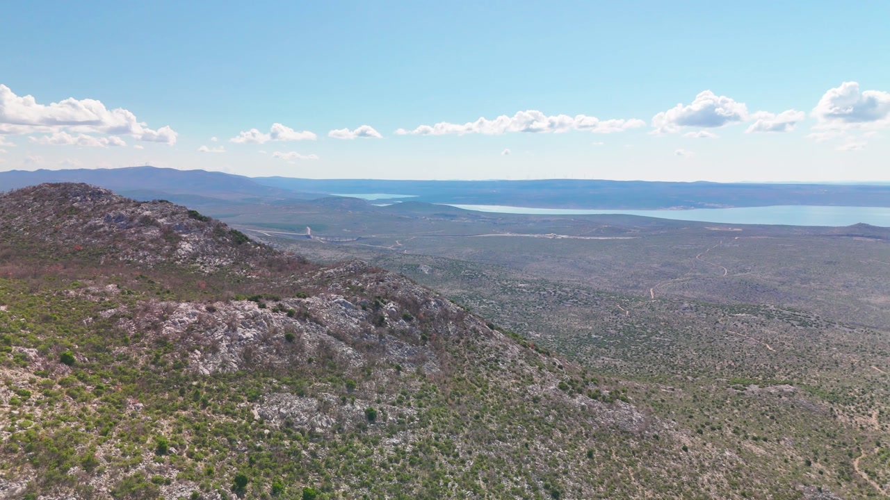 Drone turns from a dirt road toward open plains, revealing Novigradsko more and then the Adriatic Sea, with the strip of land between the two waters under clear sunny skies.