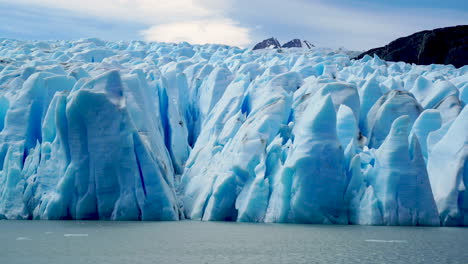 glaciar azul iluminado por el sol con grandes grietas derritiéndose, montañas distantes