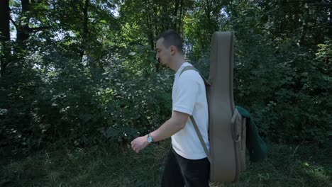 young man walking with guitar on street near forest