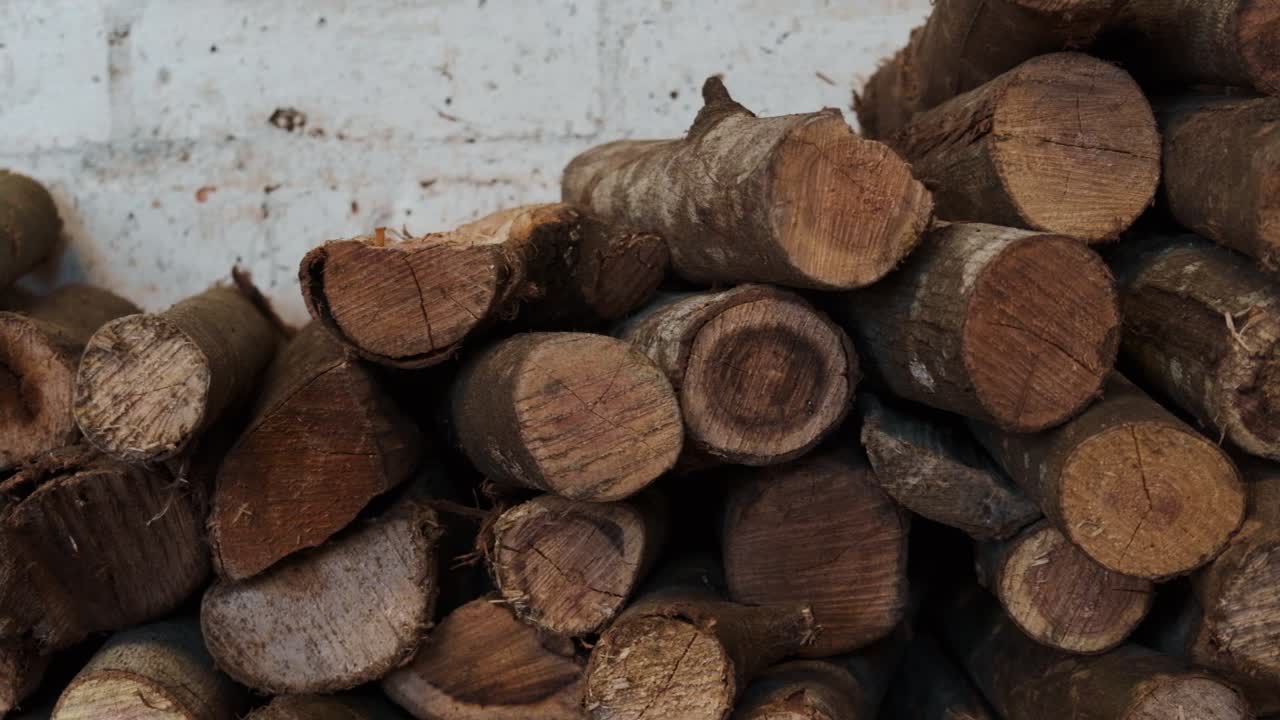 Stacked pile of firewood logs pile against white brick wall