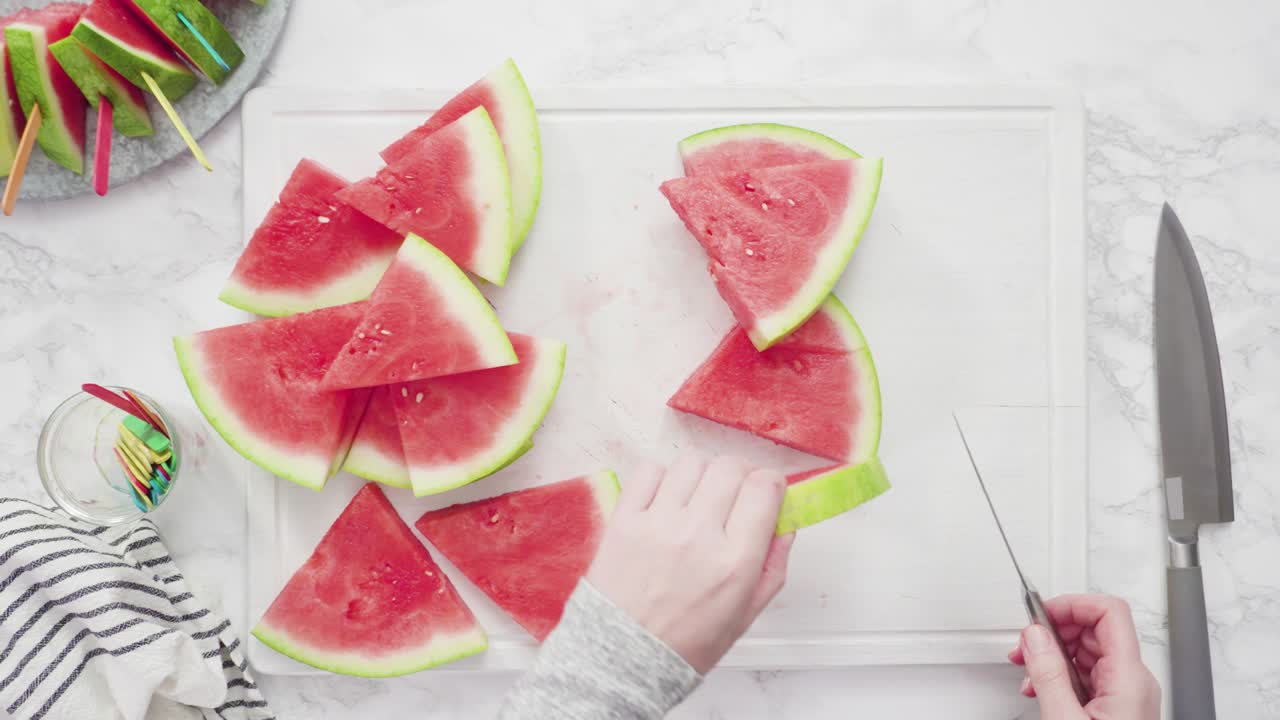 cortar la sandía roja en pedazos pequeños en una tabla de cortar blanca.