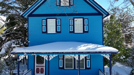 Charming-blue-Victorian-home-in-town-surrounded-by-trees-in-winter-snow