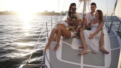 gorgeous scene of company of young happy friends sail on a yacht bow on a summer day, friends, men and women relax in the sun. beautiful, mild sunlight and urban silhuettes on the background