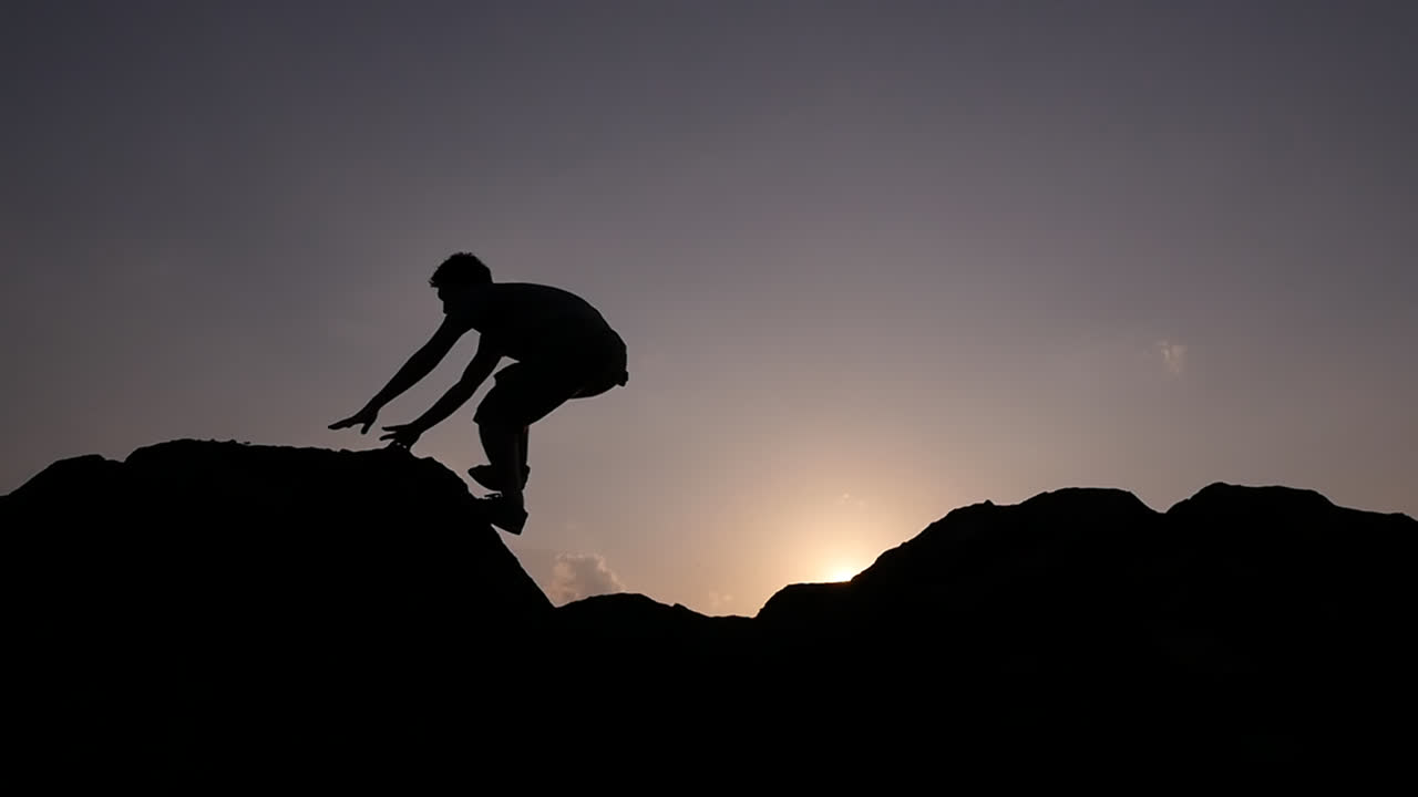 Silhouette of Man Jumping over Rocks at Sunset