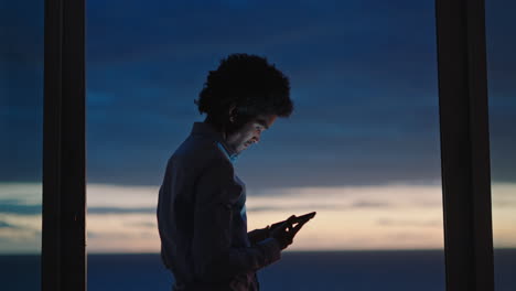 young man using smartphone in hotel room texting sharing vacation lifestyle on social media enjoying view of ocean at sunset