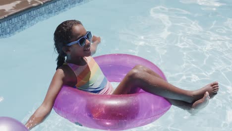 happy african american girl sitting in swim ring in swimming pool, slow motion