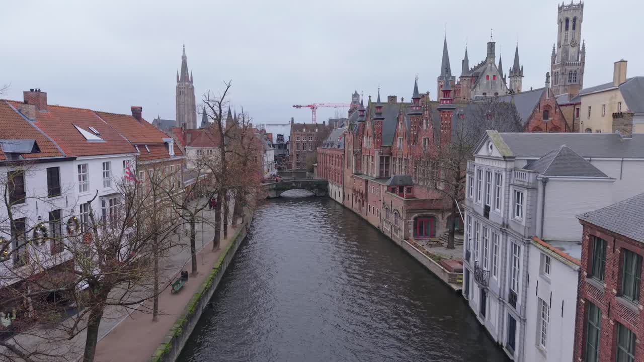 Droneoptagelse, der viser Brugges historiske kanaler og middelalderlige arkitektur i Belgien. Stemningsfuld vinteratmosfære med overskyet himmel og gamle murstensbygninger langs vandet.