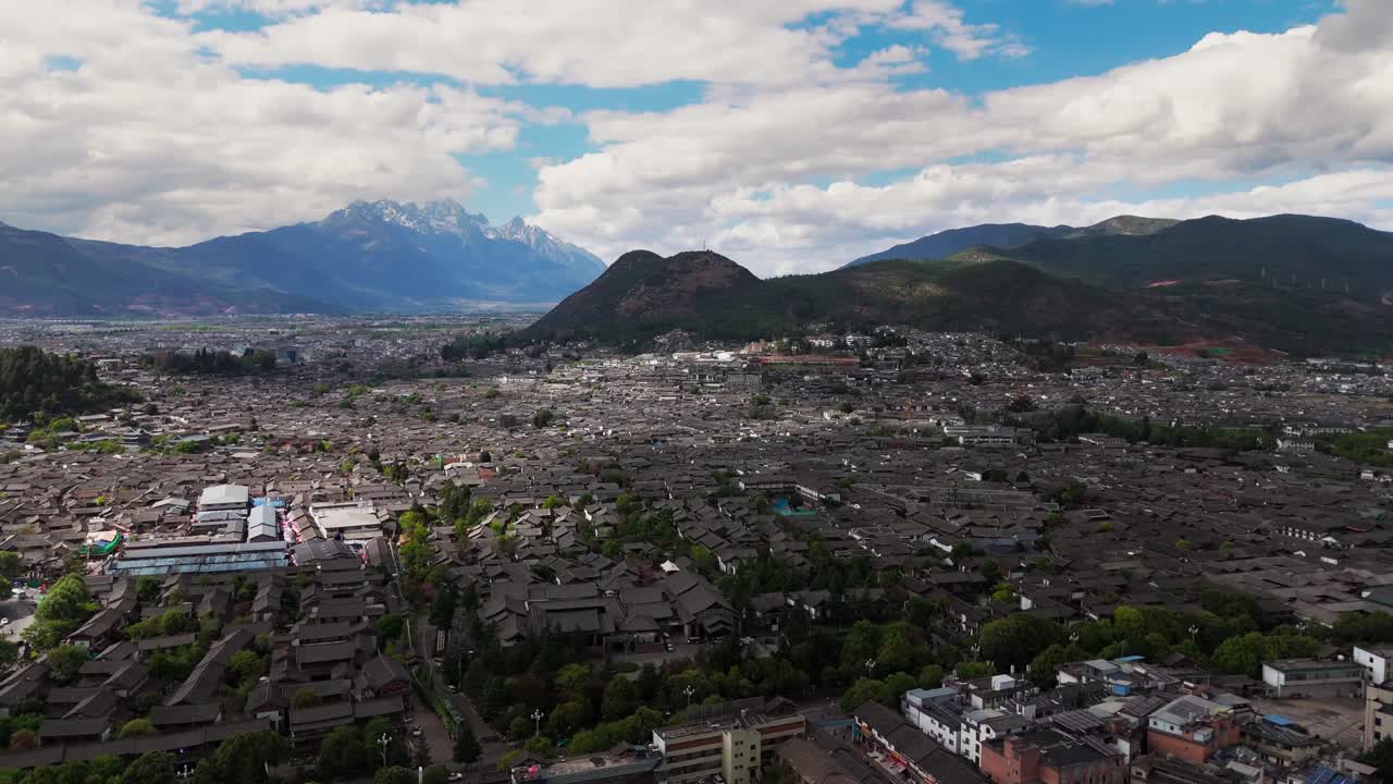 Historic Lijiang Old Town surrounded by green hills under soft clouds and late sun, orbit right with mountain backdrop