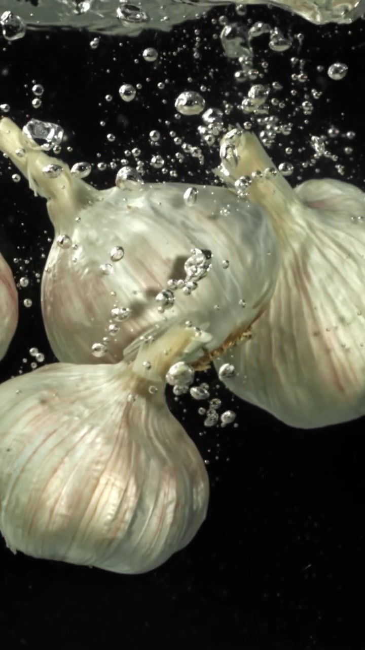Bulbi d'aglio freschi che cadono nell'acqua con bolle al rallentatore.