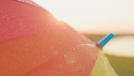 close up of a colorful umbrella covered in rain drops at sunset