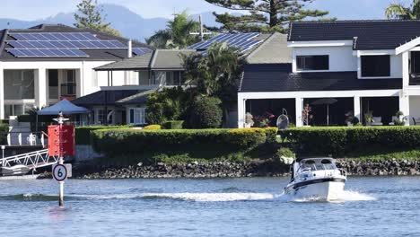 a boat moves past waterfront houses and a marker