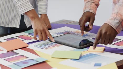 midsection of african american male and female creatives using tablet brainstorming, slow motion