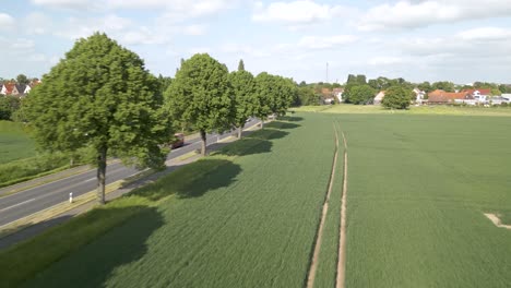aerial drone forward moving shot over cars passing by on the road surrounded by rural green farmlands in brunswick, germany on a cloudy day