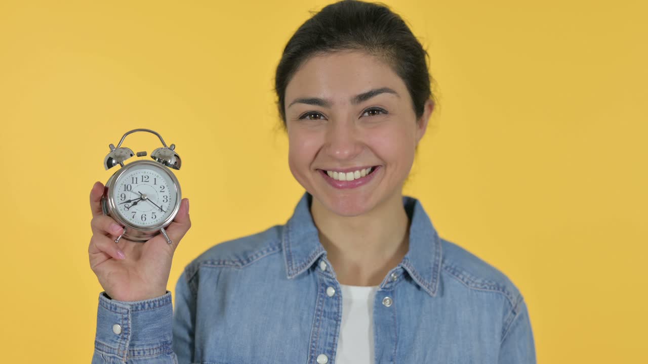 Giovane donna indiana che tiene in mano un orologio, sfondo giallo.