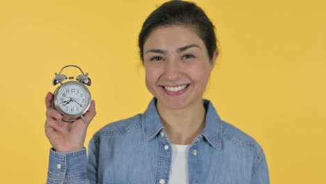 young indian woman holding a clock, yellow background