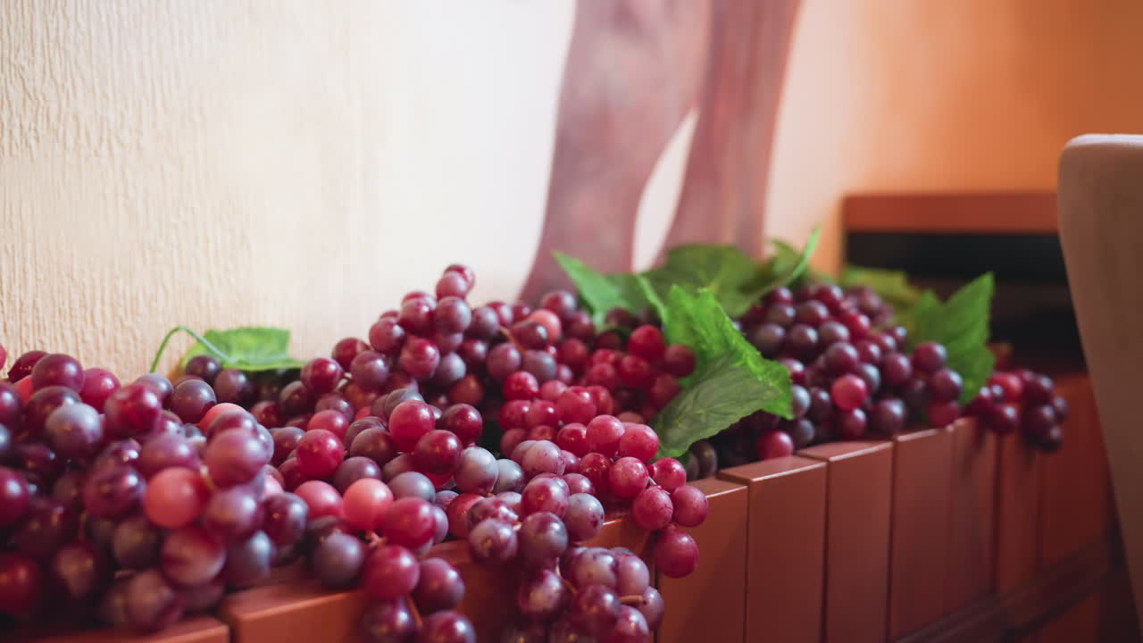 Close up display of artificial grape clusters in rich red and purple hues with green leaves arranged along wooden divider in cozy restaurant interior