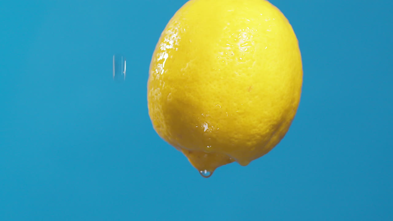 vanddråber, der løber fra en hel sur og frisk citron ned på en blå baggrund, frugt til frisk og naturlig juice, kold diætdrik med vitamin c