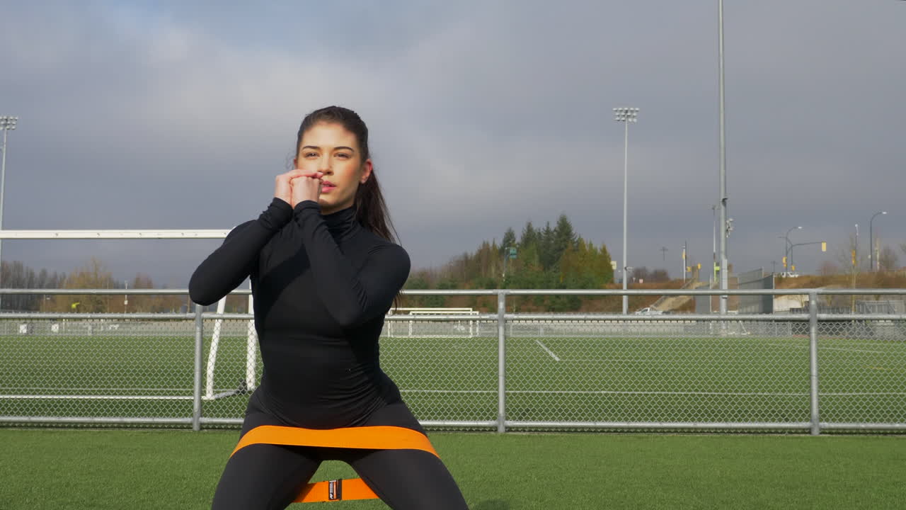 joven atlética haciendo ejercicio con una correa elástica alrededor de las piernas dobladas