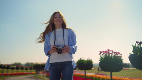 Joyful-girl-with-camera-laughing-to-photographer-in-sunny-spring-garden-outside.