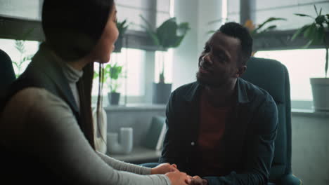 tender multiethnic couple sit on chairs hand in hand find compromise on couples therapy tender couple sit on chairs hand in hand smile talk look at each other find compromise after fight on couples therapy happy multiethnic young family on counseling session with psychotherapist