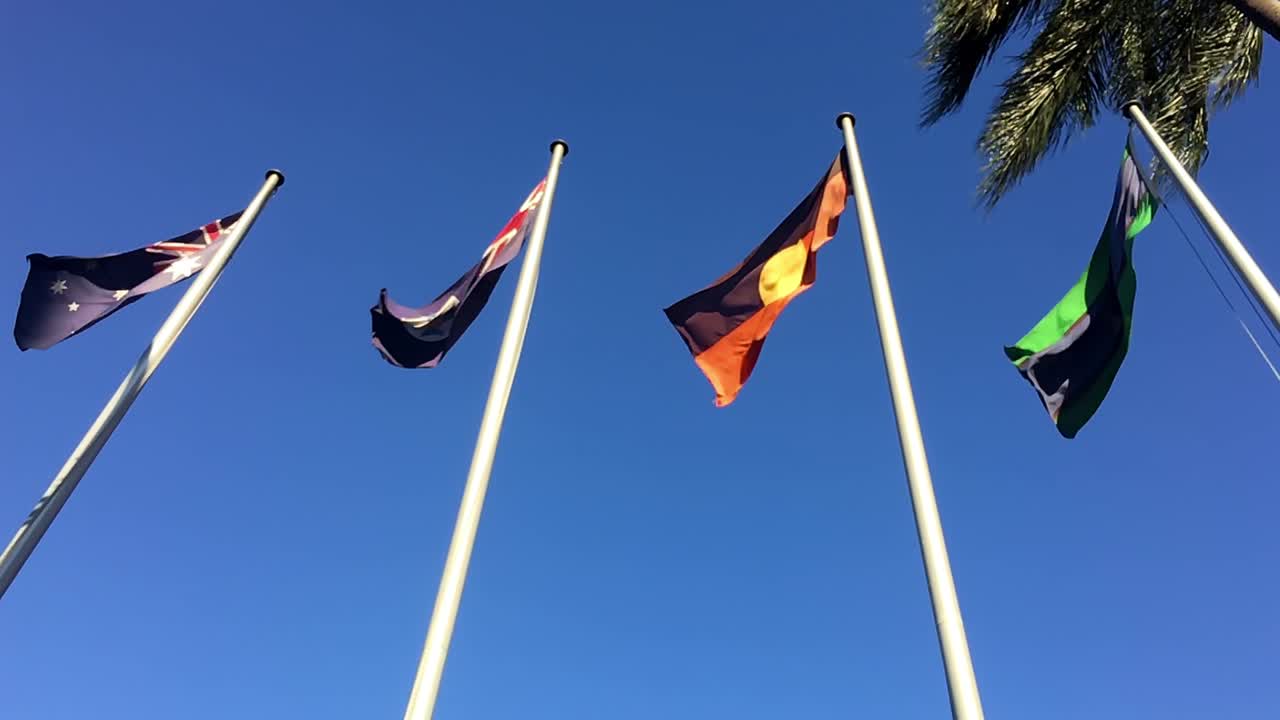 Slow motion shot of the four flags outside Queensland Parliament House fluttering in the wind, in Brisbane, Australia