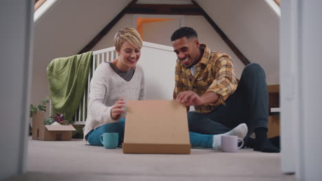 couple expecting baby eating pizza in nursery of new home together with moving in boxes