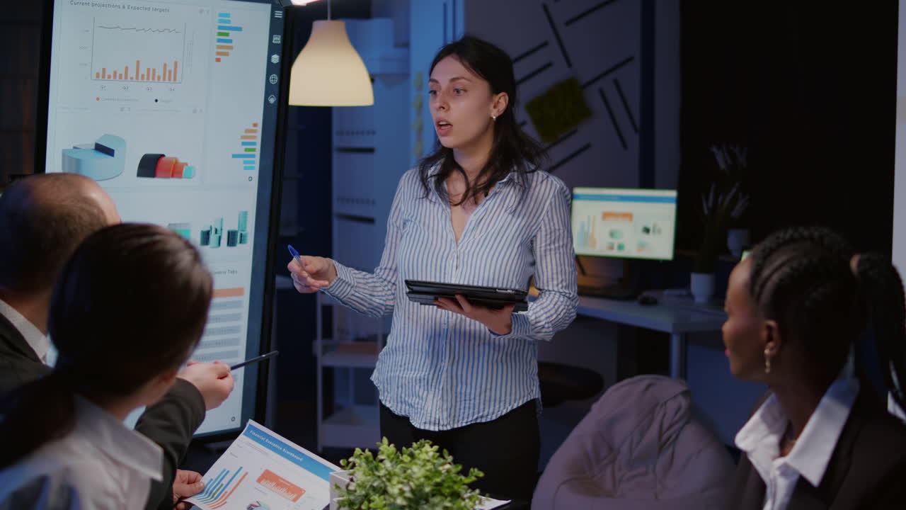 Imprenditrice maniaca del lavoro che indica la strategia finanziaria usando il monitor mentre fa gli straordinari