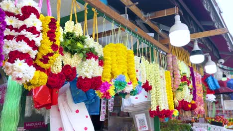 vibrant jasmine and rose garlands hang in a bustling singapore market, captured in bright daylight with smooth lateral camera movement revealing intricate floral arrangements
