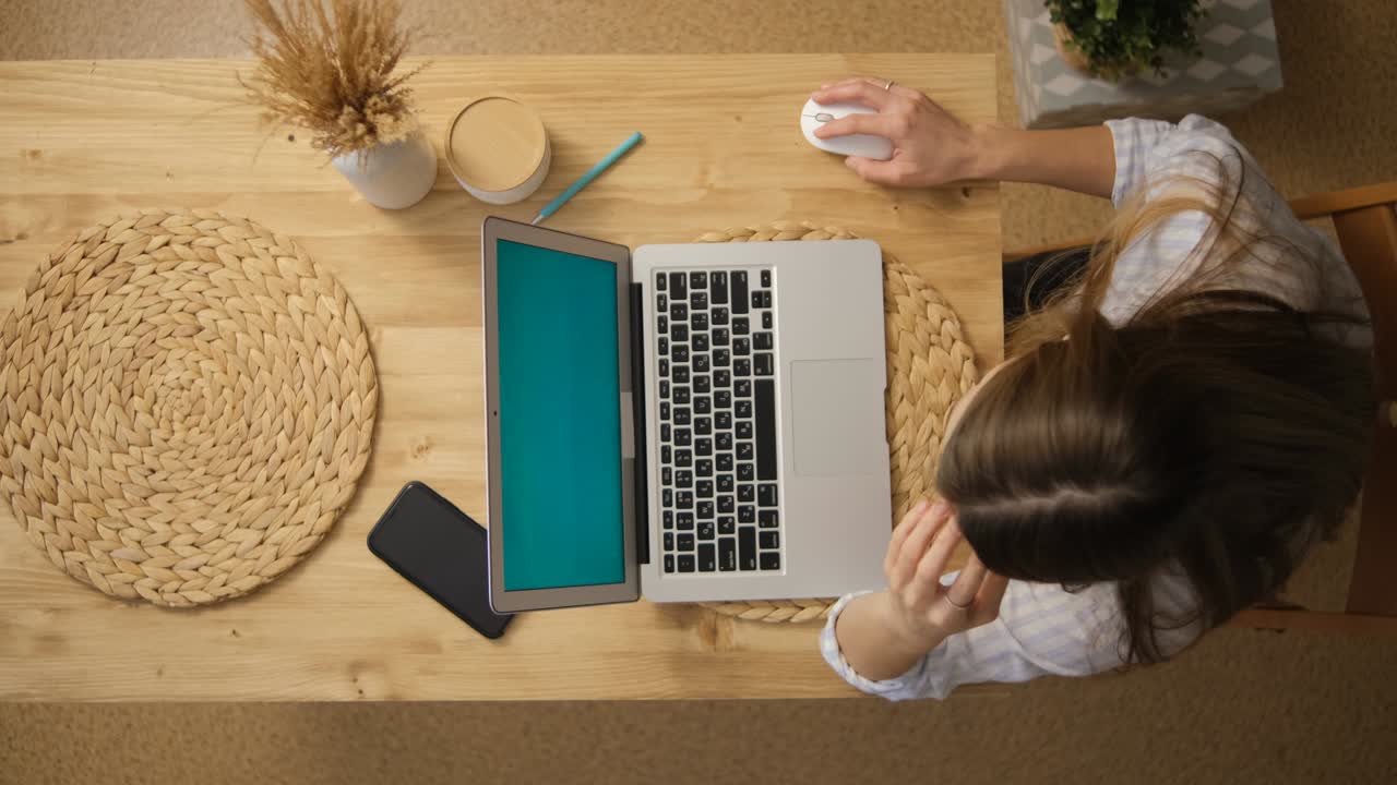 The girl works remotely on a laptop. Top view. Green laptop monitor. Beige colors. Long hair.