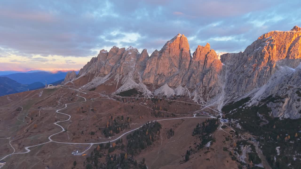 Solopgang over Gardena Pass med snoet vej og kørende bil, luftfoto
