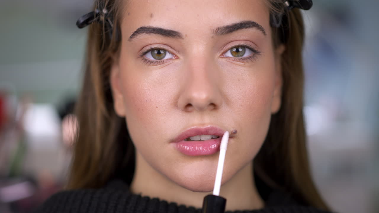 A young woman applies lip gloss