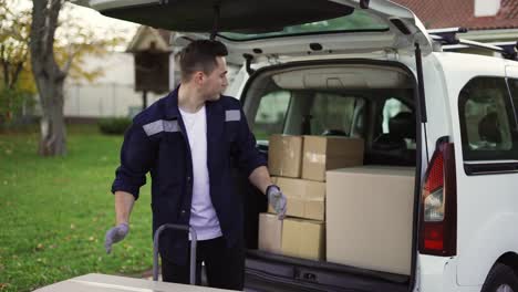 Un-Hombre-Guapo-Saca-Cajas-Del-Baúl-Y-Las-Coloca-En-Un-Carro-De-Mano.-Entrega-De-Paquetes,-Carro-De-Mano