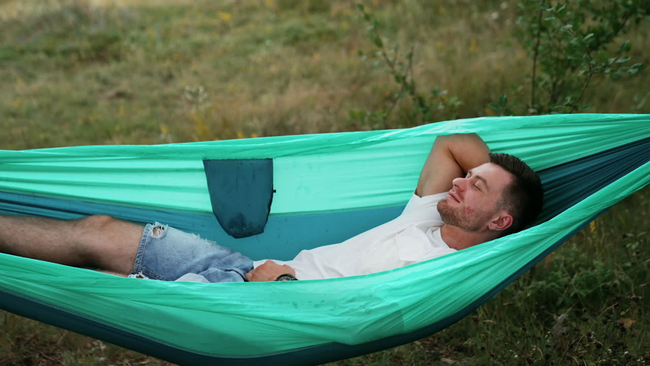 Relaxed Caucasian man swaying in hammock falling asleep. Person having rest in nature.