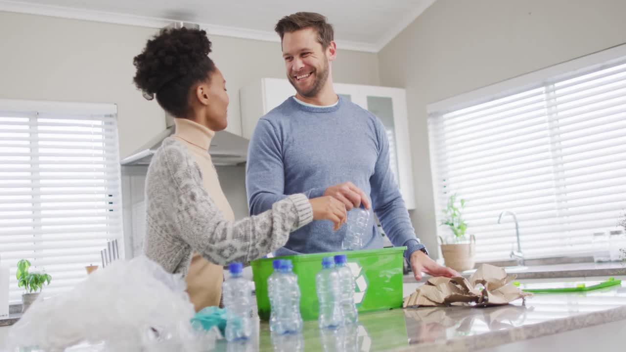 video de una feliz pareja diversa recolectando botellas de plástico para reciclar en casa