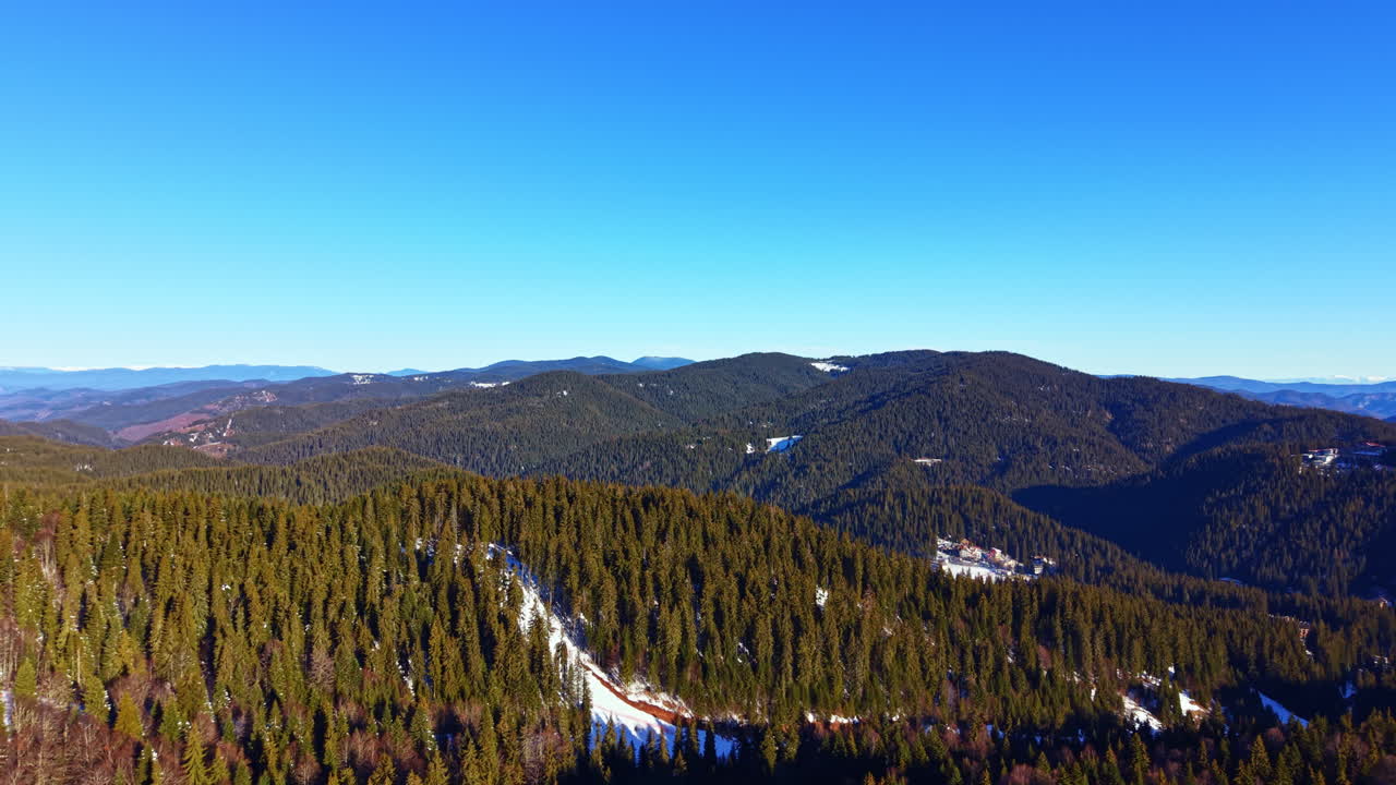 Luftfoto af et stort vinterbjergskovlandskab under en klar blå himmel.