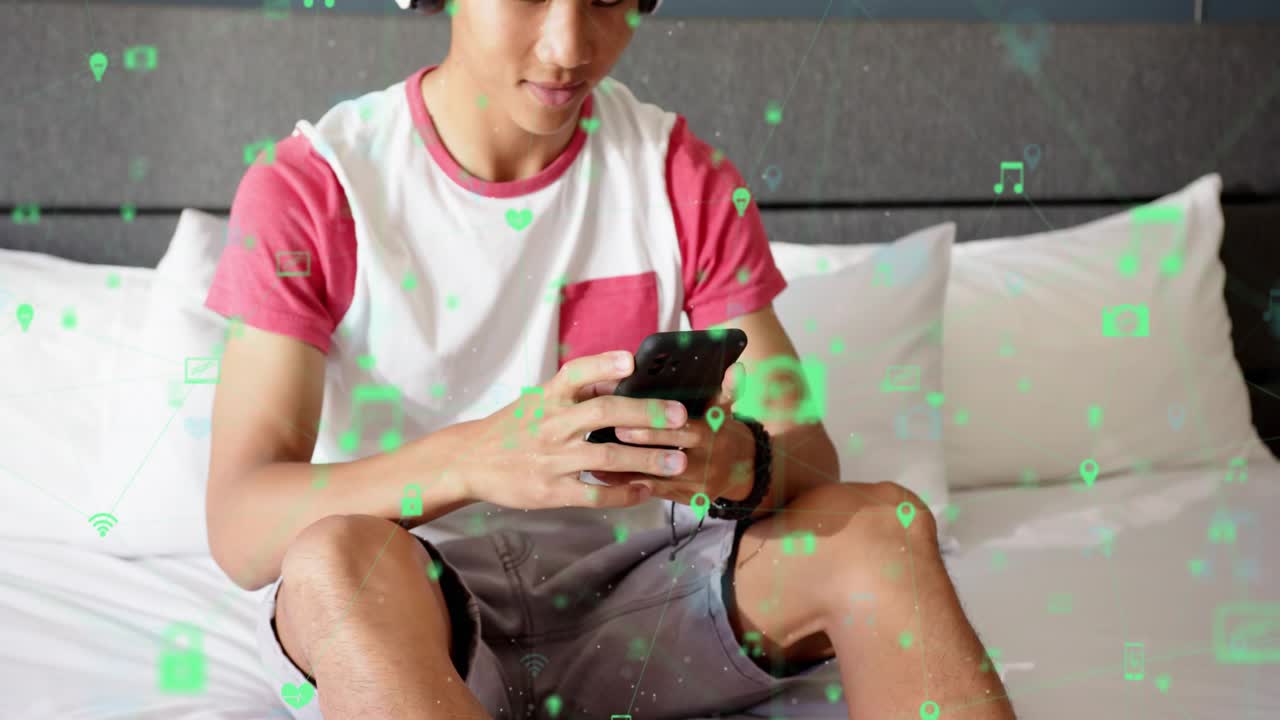Teen male reclining on bed sitting tapping smartphone to check new floating tech icons around phone