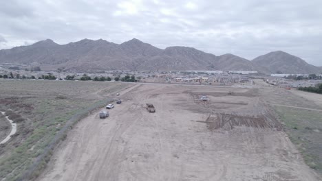 Una-Toma-Desde-Un-Dron-Observa-Una-Traílla-Elevadora-Y-Un-Camión-Cisterna-Trabajando-Juntos-Para-Preparar-El-Terreno-Para-Un-Futuro-Sitio-De-Construcción-De-Viviendas.