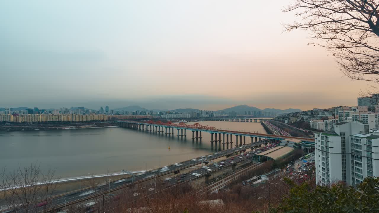 Time lapse del paesaggio urbano di Seul con traffico intenso sull'autostrada Gangbyeonbuk-ro, il Ponte Donho che attraversa il fiume Han, lo skyline degli appartamenti di Gangnam e Hannam, montagne, e un caldo e nebbioso tramonto invernale.