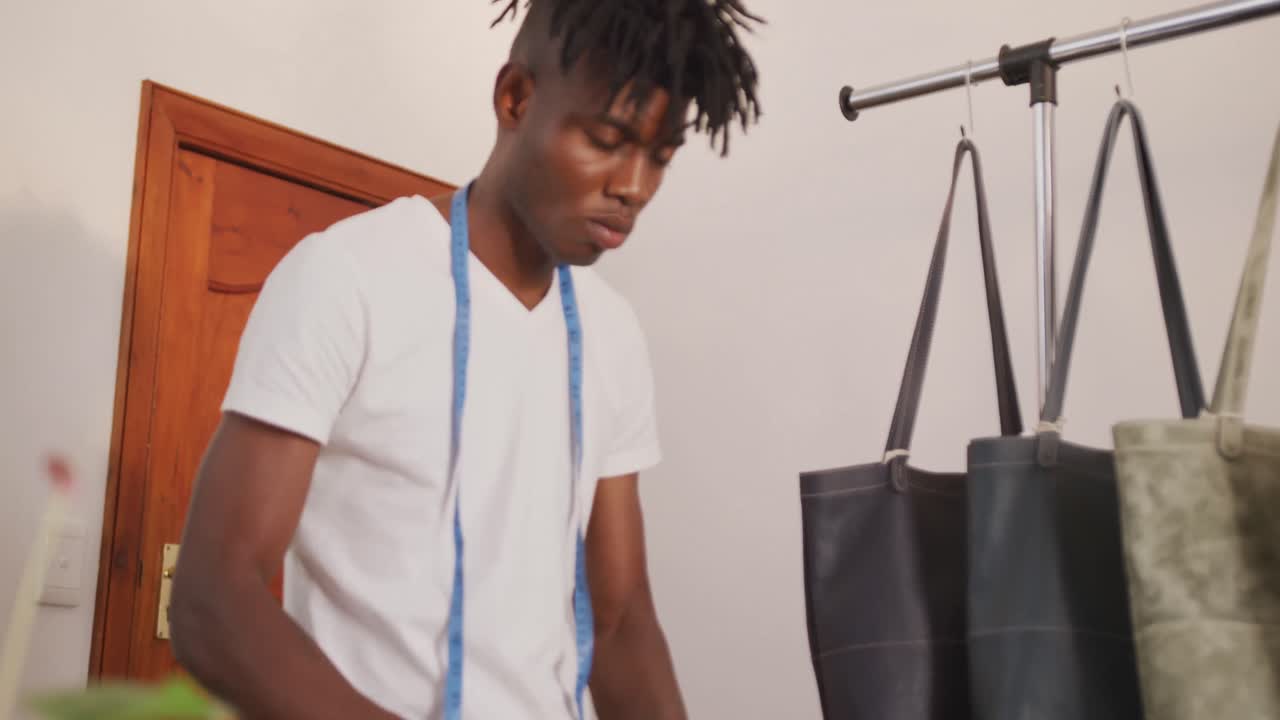 African american craftsman with dreadlocks arranging wallets and bags in leather workshop