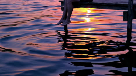 feet dangling over water at sunset
