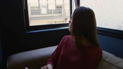 vista frontal de una joven mujer de negocios caucásica mirando por la ventana mientras usa una tableta digital 4k