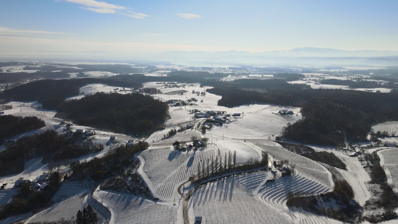 Široký záběr dronem na zasněžené kopce s vinicemi a venkovskou krajinu Slovinska