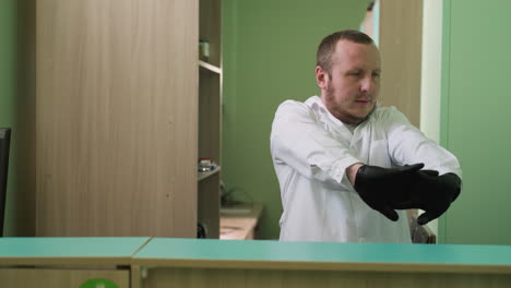 a close view of a lab technician wearing a white lab cloth and black hand gloves in a laboratory stretching his hand and turning his neck