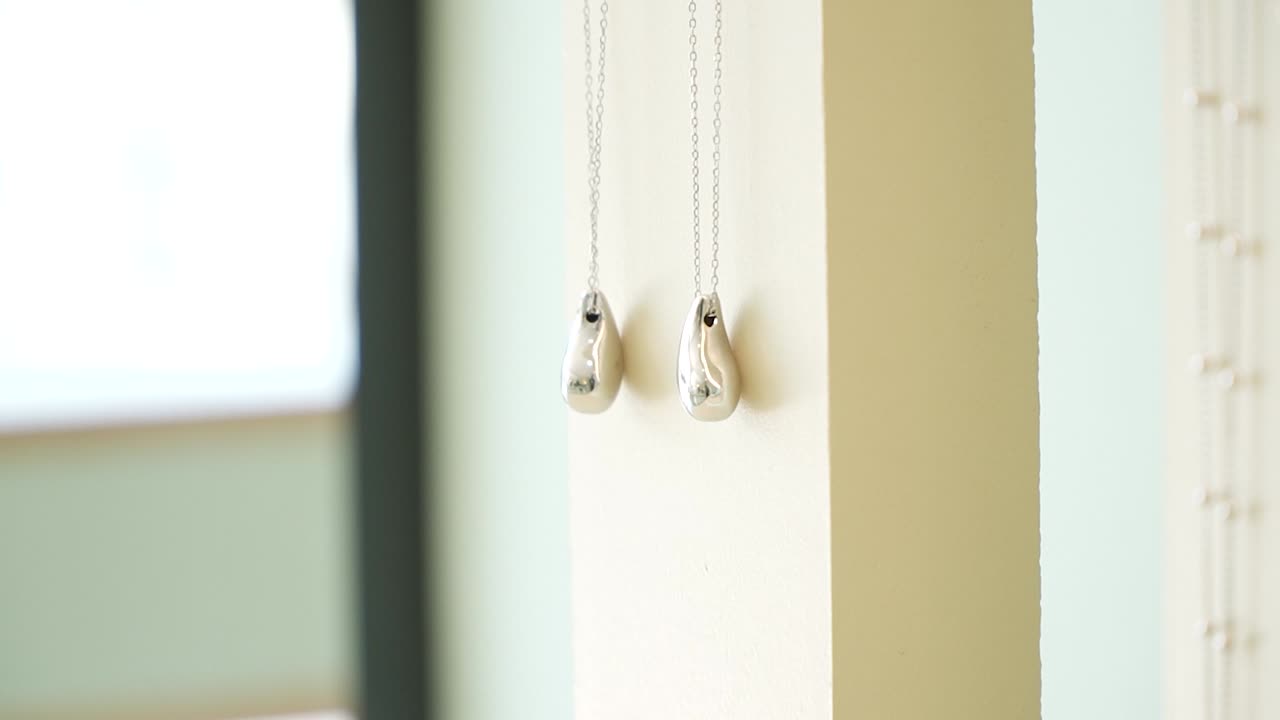 A close-up of two stunning silver pendants hanging on a wall in a beautifully lit modern room. The simple design adds elegance to the minimalist aesthetic of the space