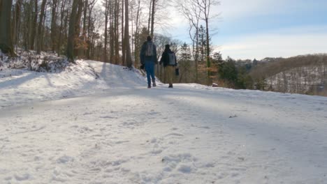 dos jóvenes excursionistas con mochilas caminando por un camino nevado durante el invierno