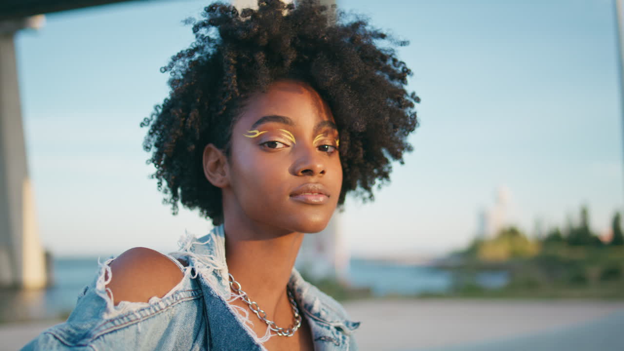 модный подросток позирует на солнечной улице с ярким современным макияжем вблизи.