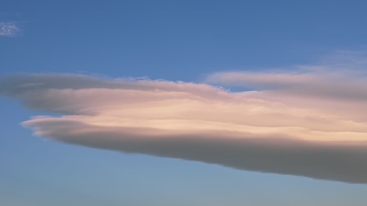 Soft, pastel-colored lenticular clouds drifting across the calm blue sky