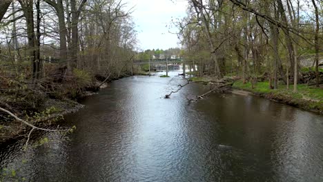 Aerial-dolly-upstream-calm-river-with-fallen-trees-before-leaves-are-on-trees